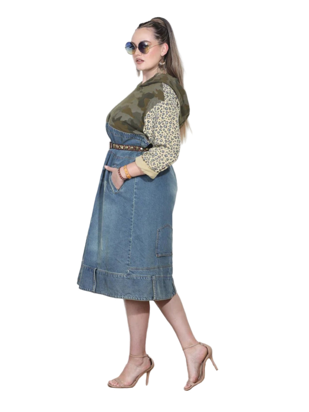 Woman wearing a green top and blue denim skirt against a white wall.