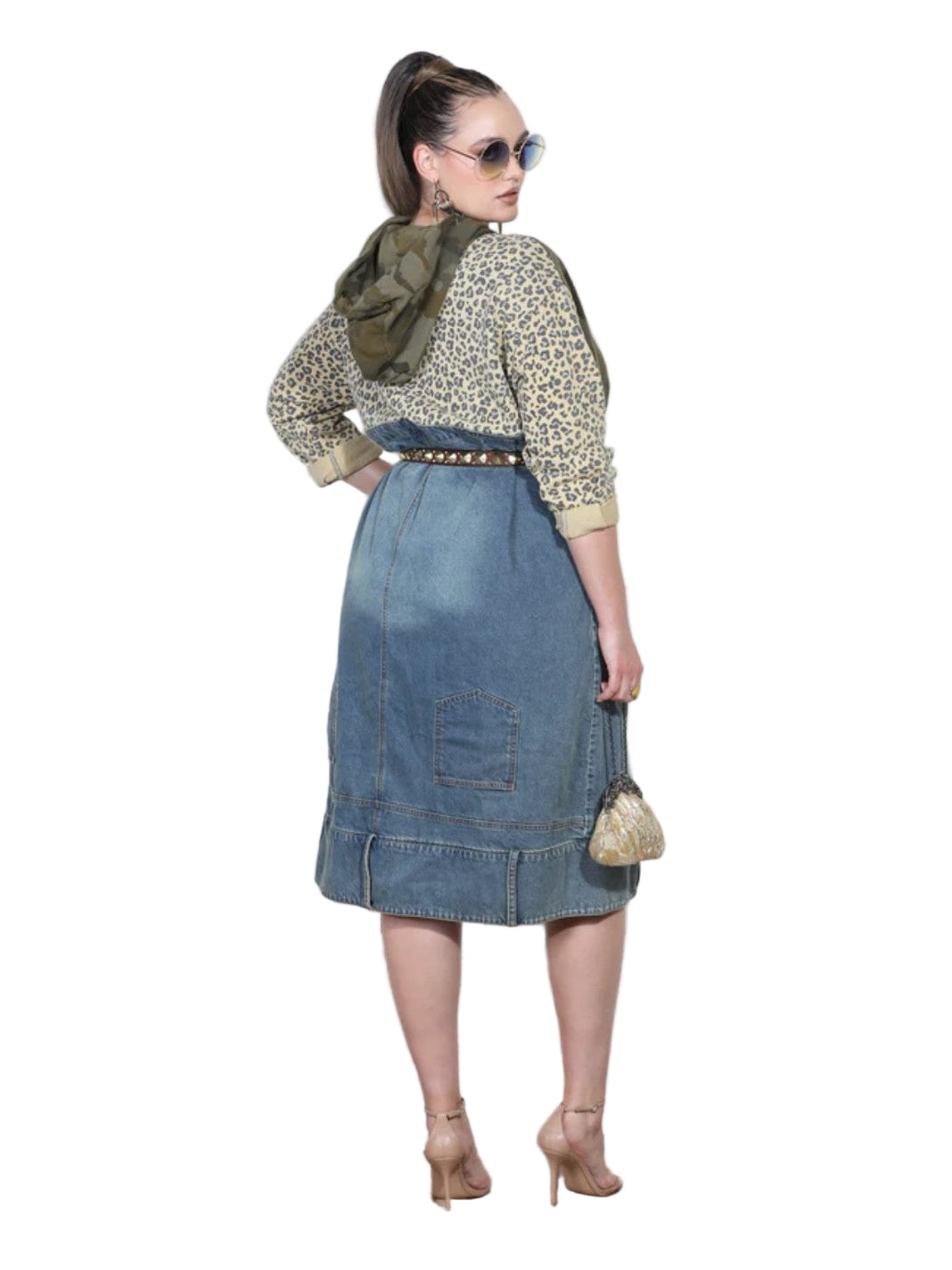 Woman wearing a floral blouse, denim skirt, and sunglasses against a white wall.